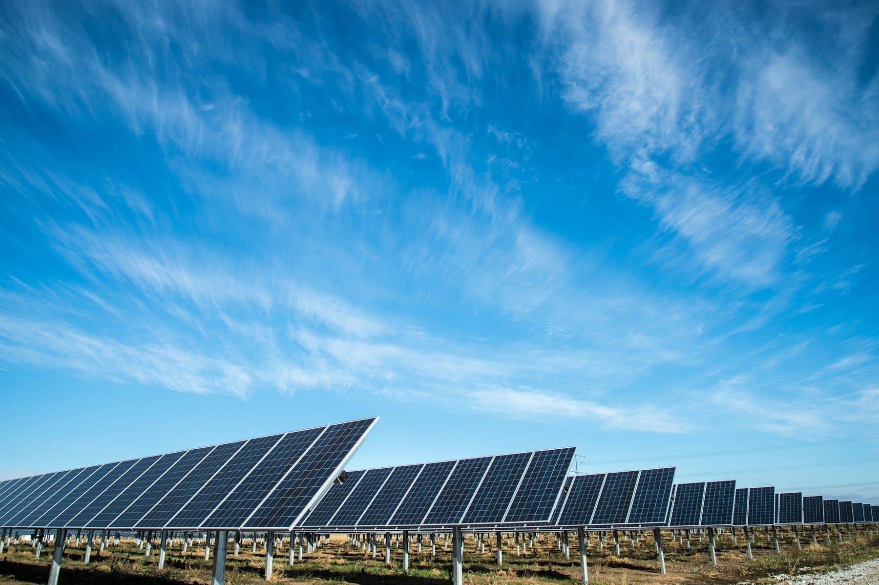 Solar field under a bright blue sky with streaked clouds