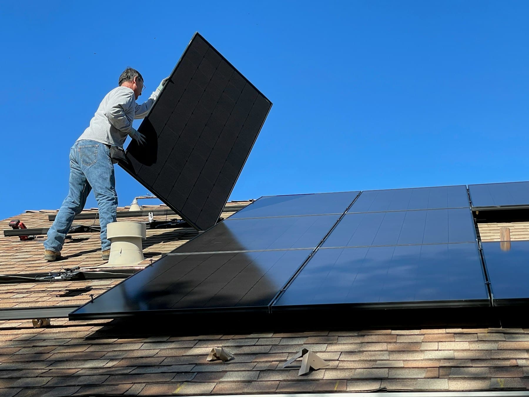 Installer fitting a solar panel on a house roof under a clear blue sky